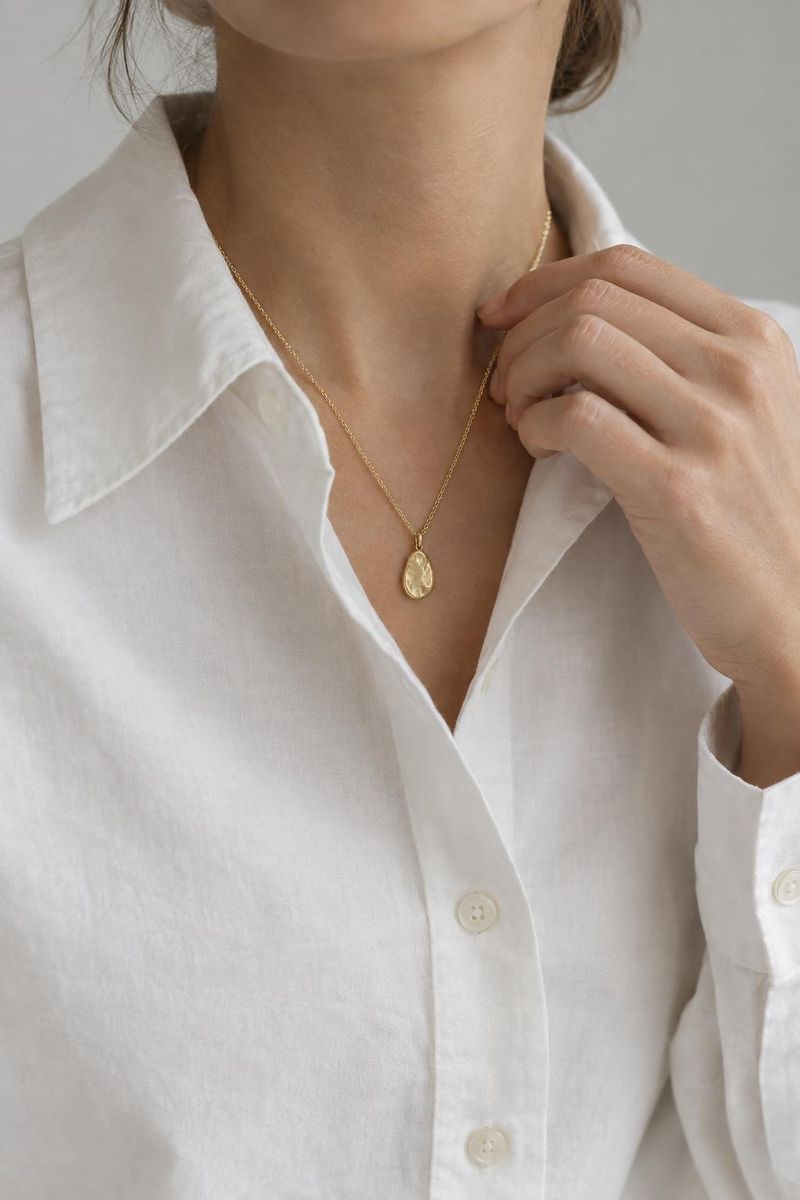 Halsband i guld på kvinna i vit blus